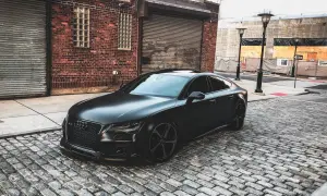 Czarny matowy samochód Audi RS7 zaparkowany na brukowanej ulicy przed ceglanym budynkiem.