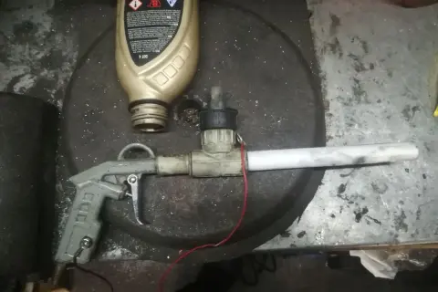 Domowy pistolet do malowania proszkowego z butelką płynu i elementami instalacji.