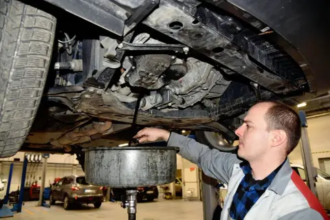 Mechanik spuszcza olej silnikowy z samochodu do miski.