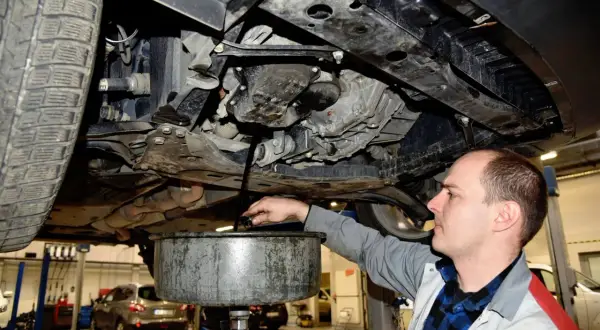 Mechanik spuszcza olej silnikowy z samochodu do miski.