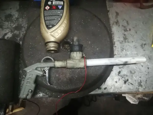 Domowy pistolet do malowania proszkowego z butelką płynu i elementami instalacji.