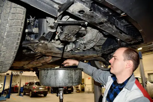 Mechanik spuszcza olej silnikowy z samochodu do miski.